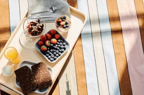 Top view of a healthy breakfast tray with fruits, bread, and juice on a striped tablecloth.