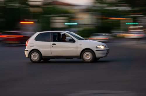 A white car speeds through a city street in the evening, showcasing motion blur.