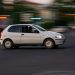 A white car speeds through a city street in the evening, showcasing motion blur.